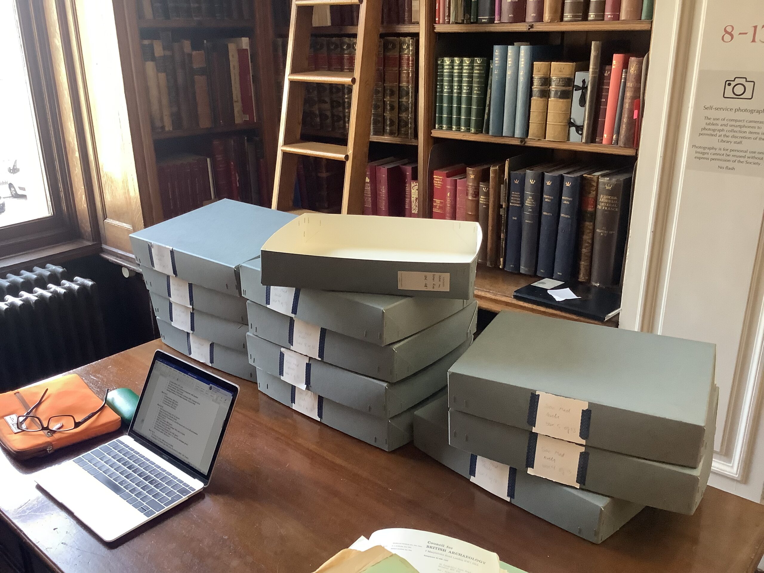 Blue archive boxes arranged in three piles on a large wooden desk.